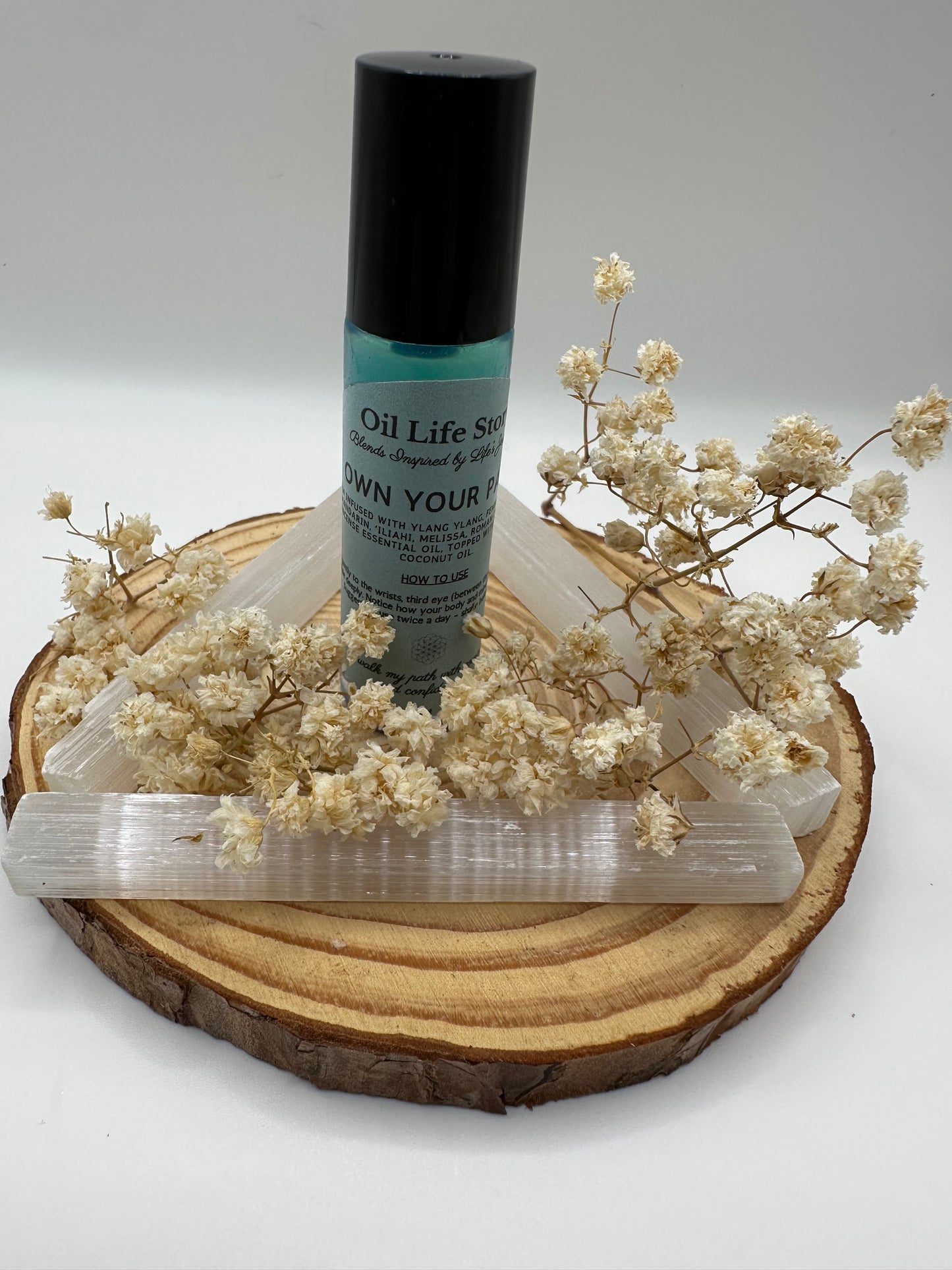 Own Your Path essential oil blend with white dried flowers and crystals on a wooden plate
