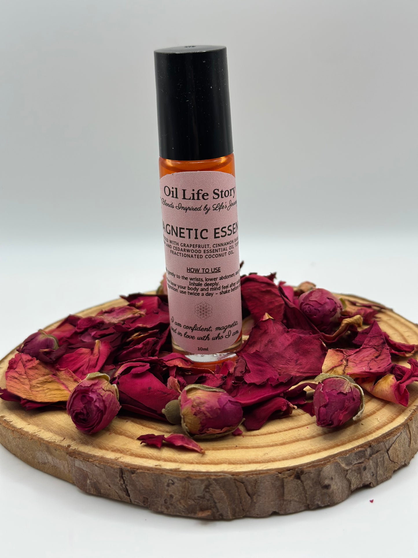 Magnetic Essence essential oil blend on a wooden plate, surrounded by dried red rosebuds