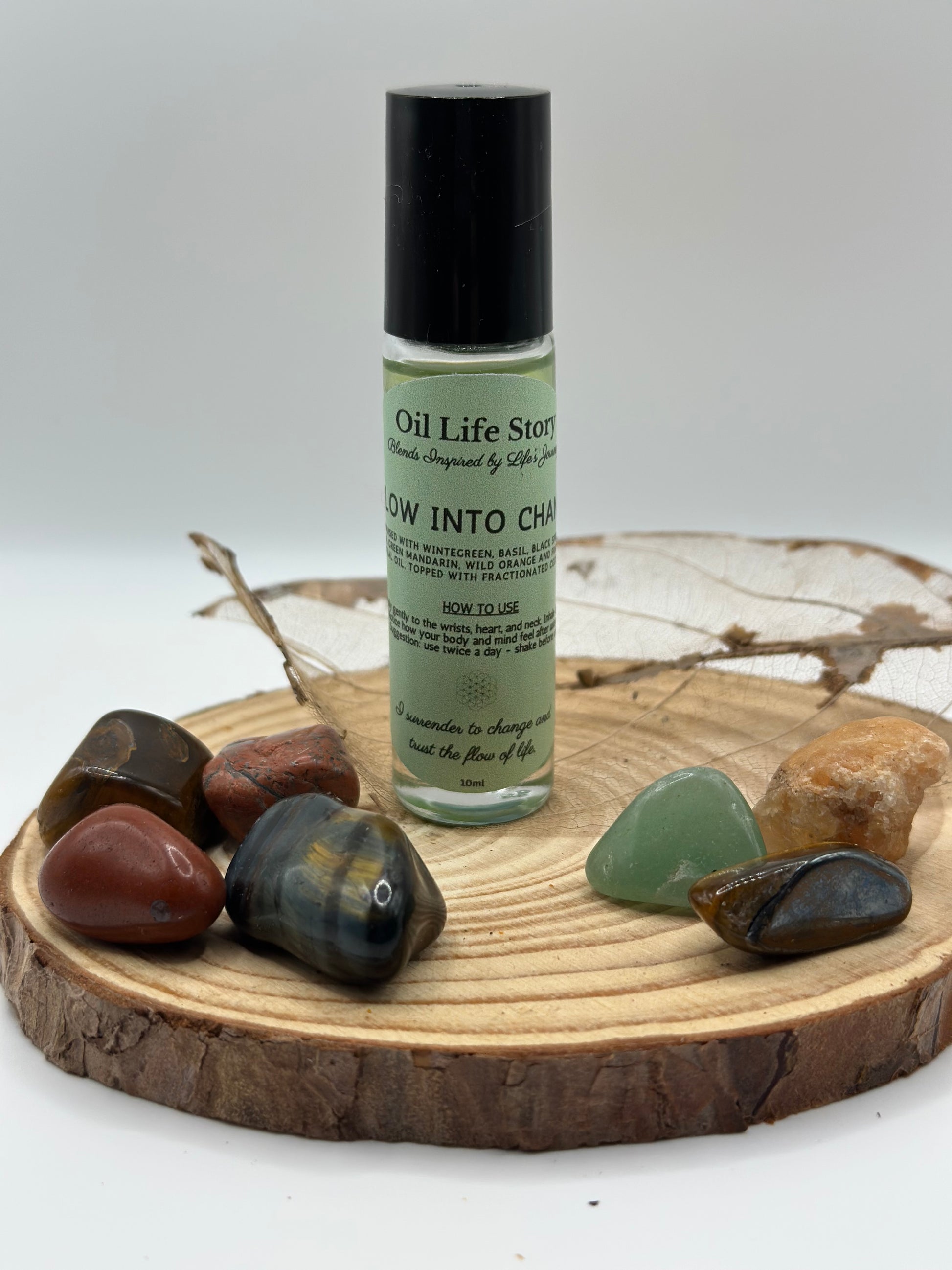Flow Into Change essential oil blend with healing crystals and a small branch on a wooden plate