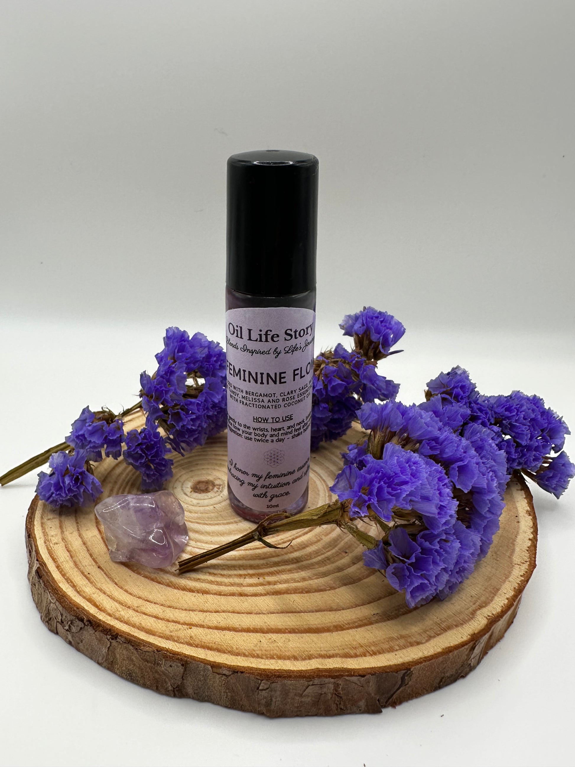 Feminine Flow essential oil blend with purple dried flowers on a wooden plate