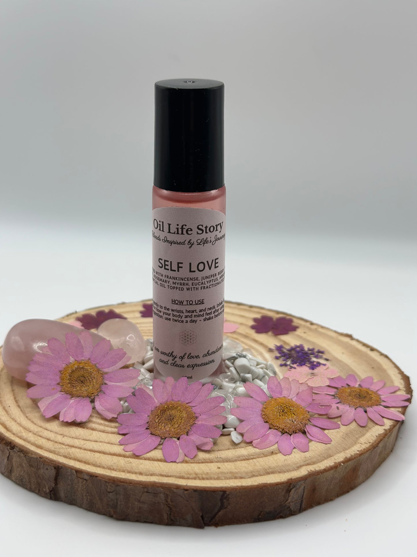 Self Love essential oil blend with pink flowers and rose quartz on a natural wood plate