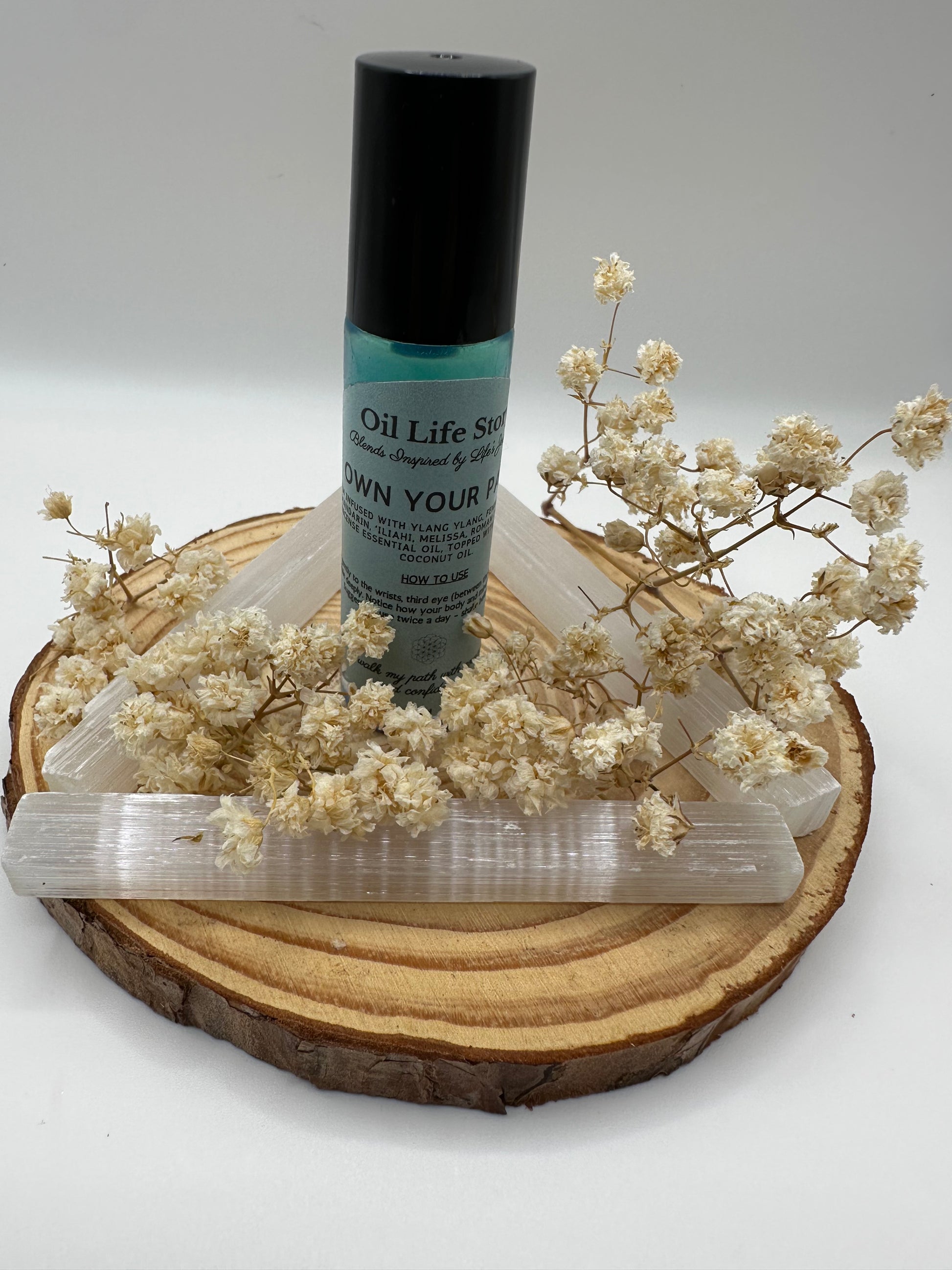 Own Your Path essential oil blend with white dried flowers and crystals on a wooden plate